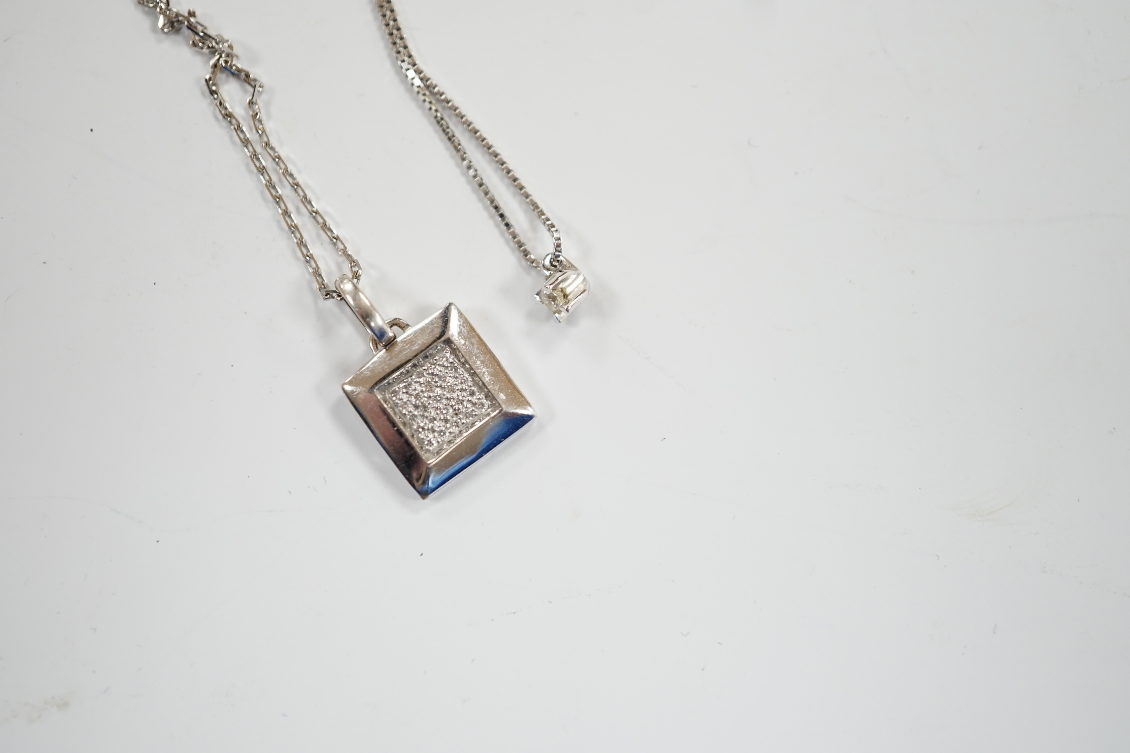 A modern Italian 18k white metal and diamond chip set pendant, on an 18k chain, 42cm and a white metal and diamond chip set square cluster pendant on an 18k chain, gross weight 6 grams.